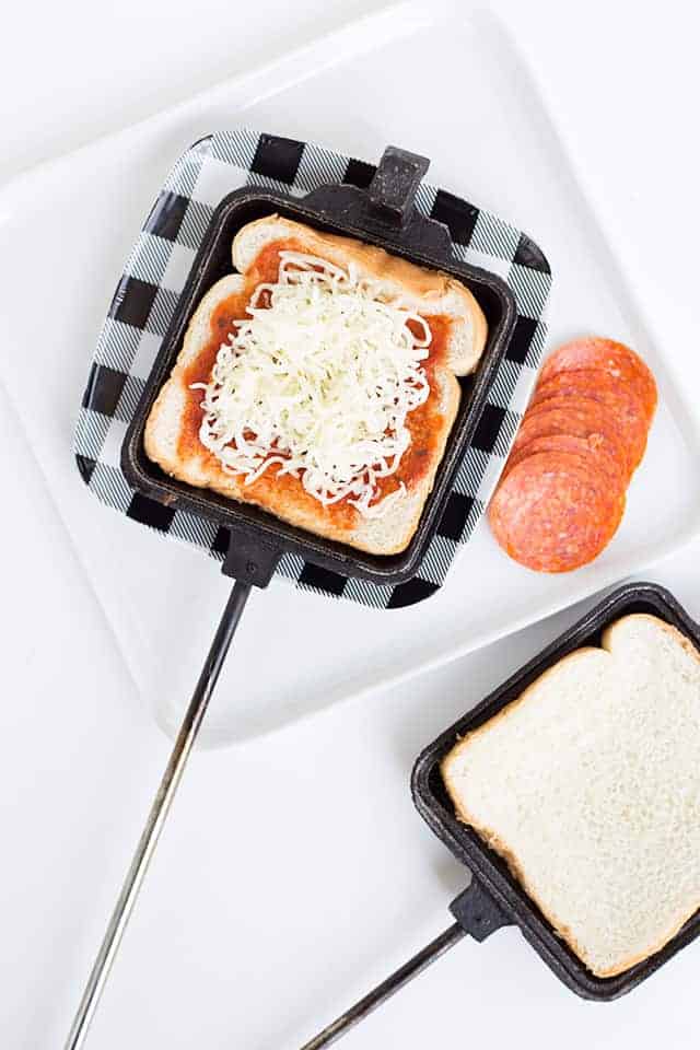 Pizza Mountain Pies - These delicious pizza mountain pies are the perfect treat while camping! These pizza mountain pies are made over the campfire coals with a pie iron. They take minutes to make and are the most amazing pizza pies you'll have! Enjoy the crunchy, buttery outside and the gooey cheese and pepperoni pizza inside. #cookiedoughandovenmitt #camping #campingrecipes #pizza adding cheese to the pizza mountain pie maker