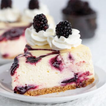 Slice of blackberry cheesecake on white plate with blackberries in background