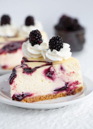 Slice of blackberry cheesecake on white plate with blackberries in background