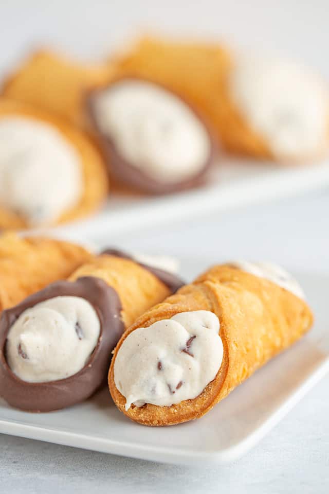 close up on a cannoli on a white plate on a white surface