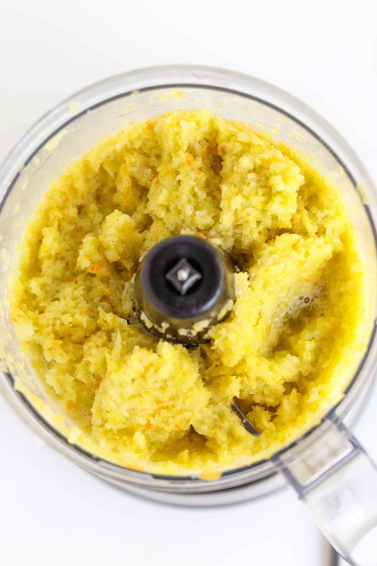 Chopped yellow Hot Pepper Butter mixture in a food processor, viewed from above, with metal blade visible at the center.