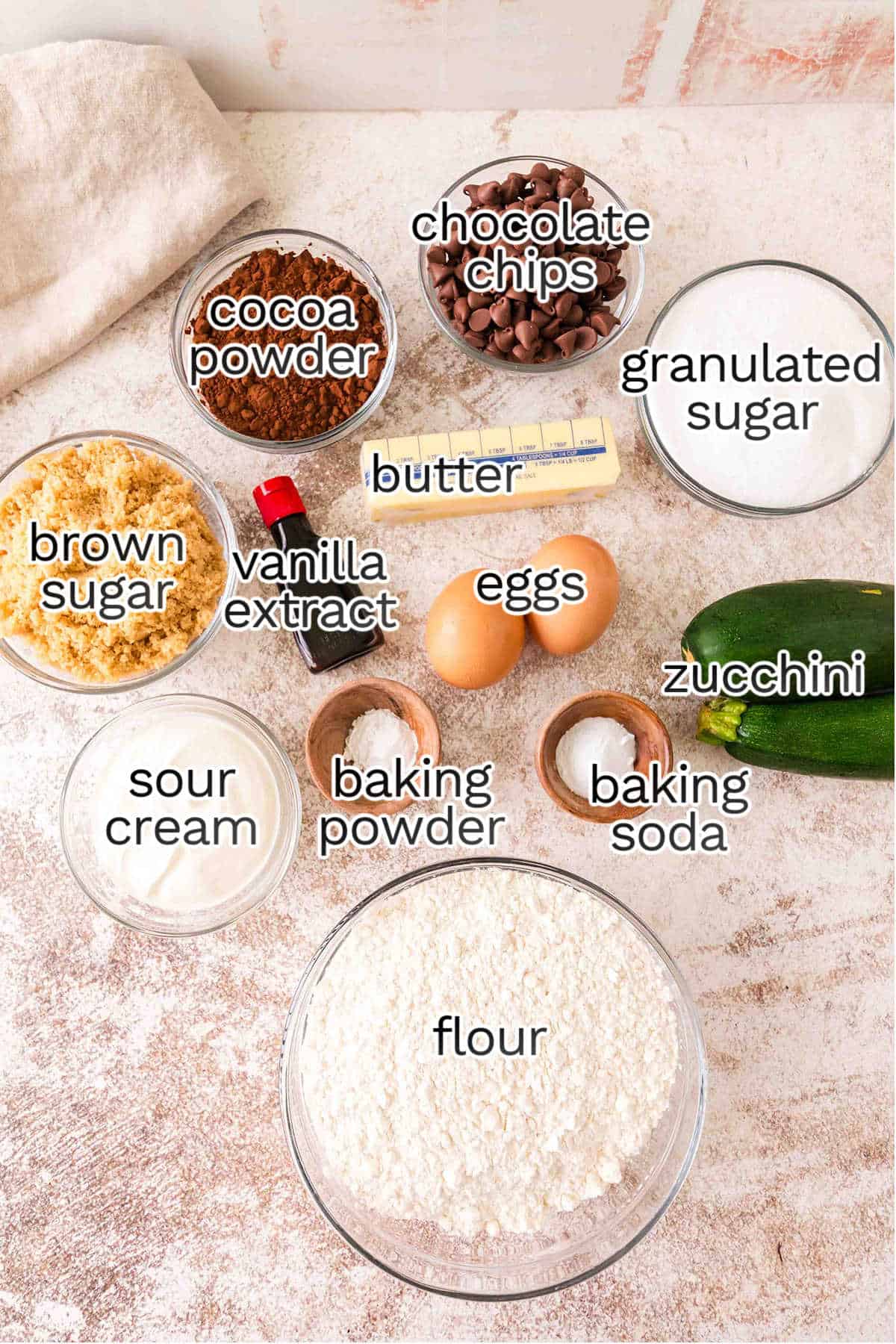 Various baking ingredients, like flour, sugars, cocoa powder, chocolate chips, and zucchini, come together to create a decadent Triple Chocolate Zucchini Bundt Cake. Butter, eggs, sour cream, vanilla extract, baking powder and soda complete the mix.
