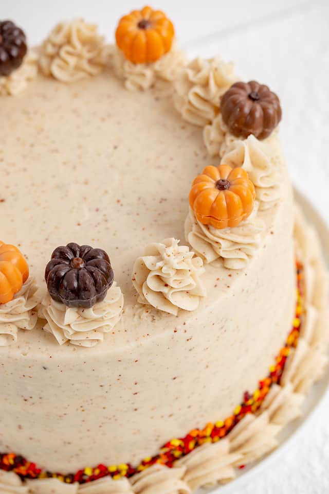 Pumpkin Cake Recipe - This moist Pumpkin Spice Cake with Brown Butter Frosting is one of the tastiest fall desserts! The brown butter frosting has specks in it and tastes sweet and nutty. The pumpkin cake is packed full of spices and topped with adorable chocolate pumpkin truffles. #pumpkin #cake #falldesserts #cookiedoughandovenmitt close up of pumpkin truffles on top of a pumpkin spice cake