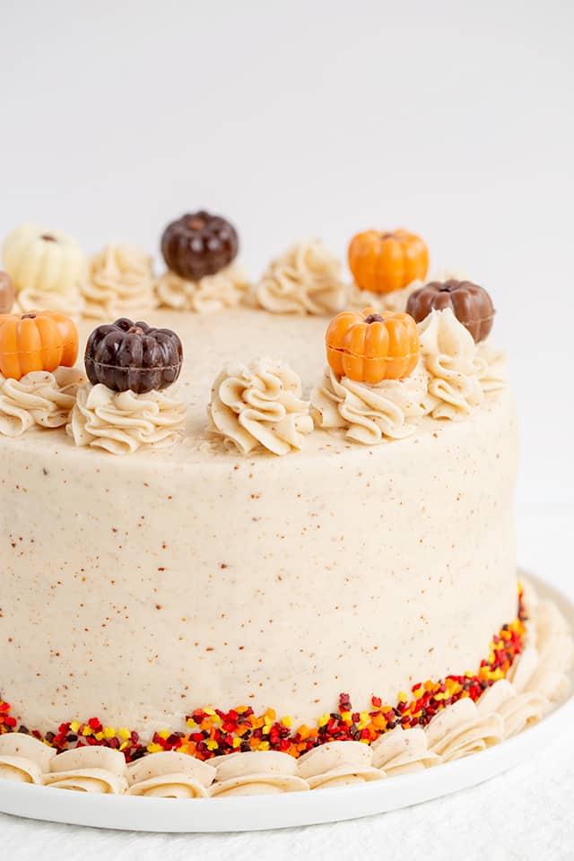 Pumpkin Cake Recipe - This moist Pumpkin Spice Cake with Brown Butter Frosting is one of the tastiest fall desserts! The brown butter frosting has specks in it and tastes sweet and nutty. The pumpkin cake is packed full of spices and topped with adorable chocolate pumpkin truffles. #pumpkin #cake #falldesserts #cookiedoughandovenmitt pumpkin cake recipe with white background and white serving plate