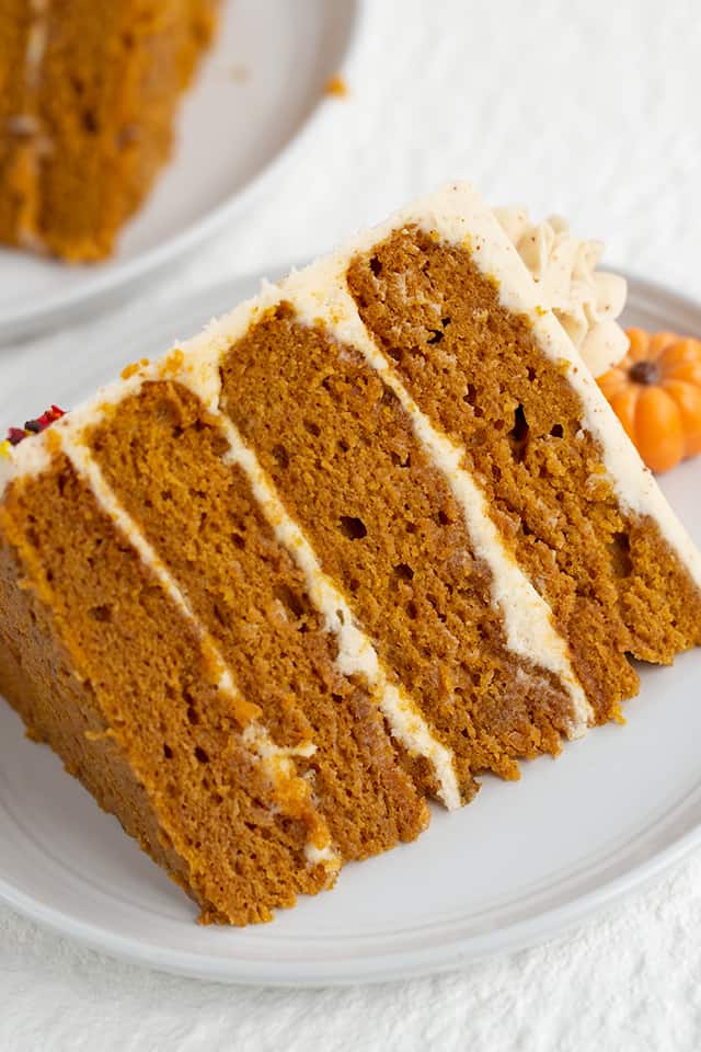 Pumpkin Cake Recipe - This moist Pumpkin Spice Cake with Brown Butter Frosting is one of the tastiest fall desserts! The brown butter frosting has specks in it and tastes sweet and nutty. The pumpkin cake is packed full of spices and topped with adorable chocolate pumpkin truffles. #pumpkin #cake #falldesserts #cookiedoughandovenmitt close up of slice of pumpkin spice cake