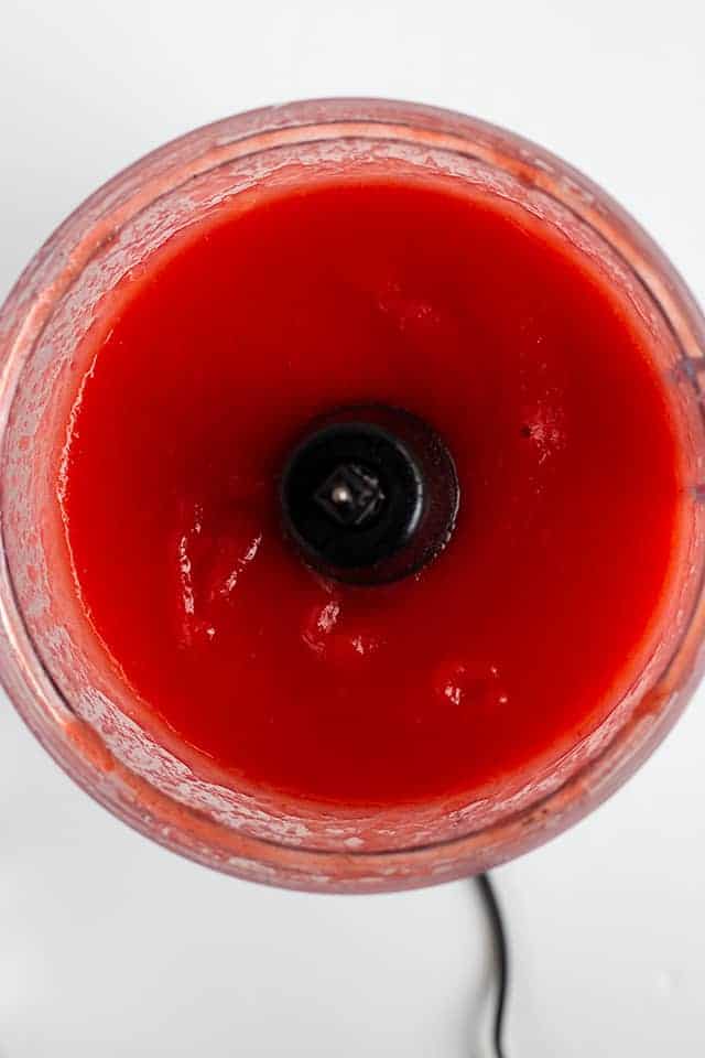 Red Hot Applesauce - This red hot applesauce is bright red and packed full of cinnamon flavor! It's such a quick and easy fall recipe to make. The recipe works great with any apple! Who knew applesauce could be so pretty and tasty? #applesauce #cinnmaonapplesauce #cookiedoughandovenmitt #fallrecipes red hot applesauce being pulsed in a food processor