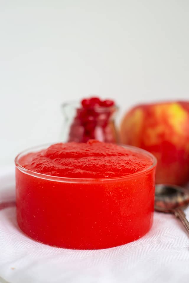 red hot applesauce in a glass bowl with a white fabric, candies, and apple