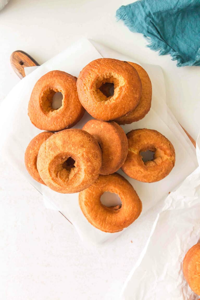 A pile of plain, golden-brown homemade cake donuts arranged on a piece of parchment paper on a white surface.