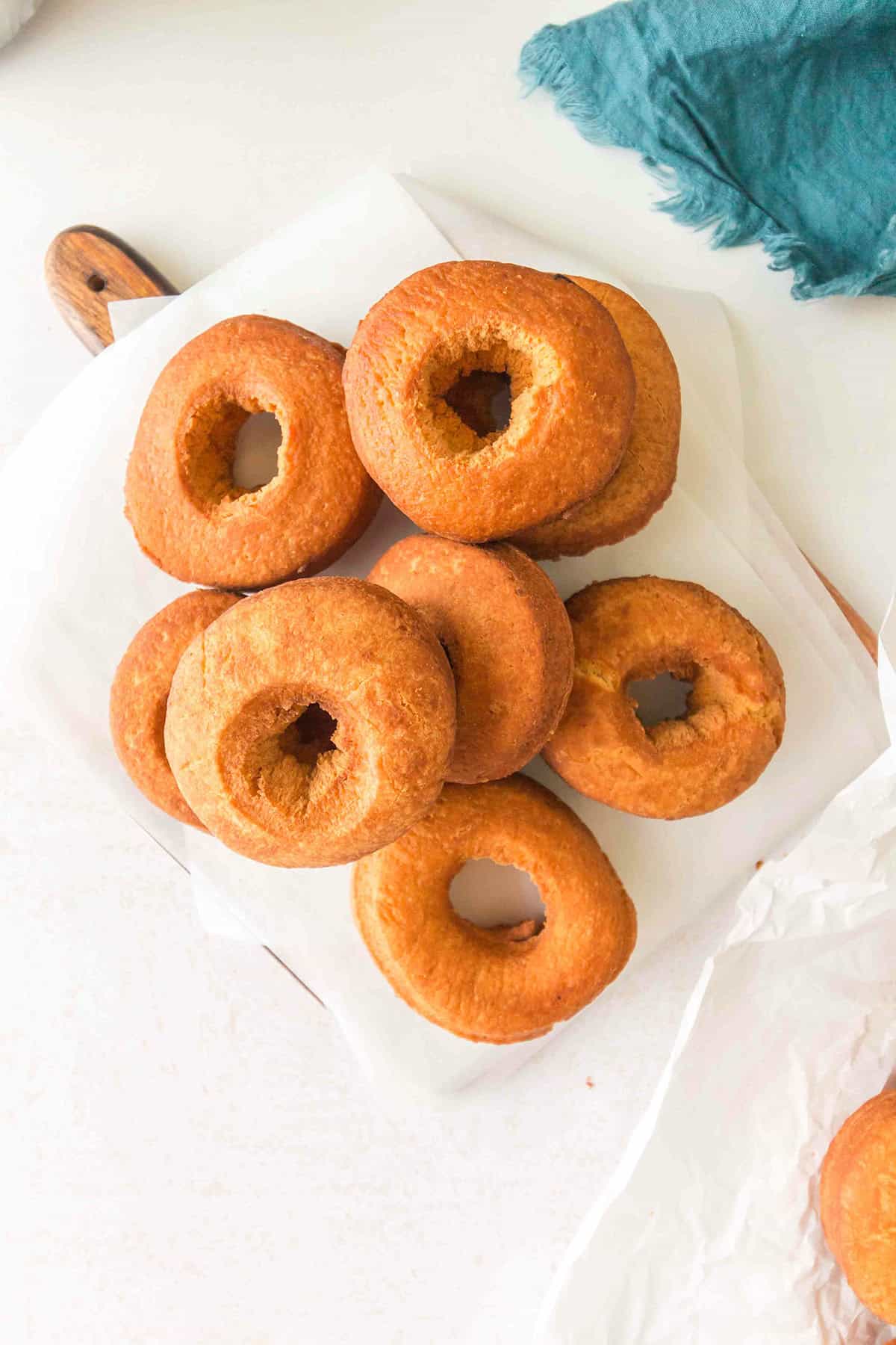 A pile of plain, golden-brown homemade cake donuts arranged on a piece of parchment paper on a white surface.