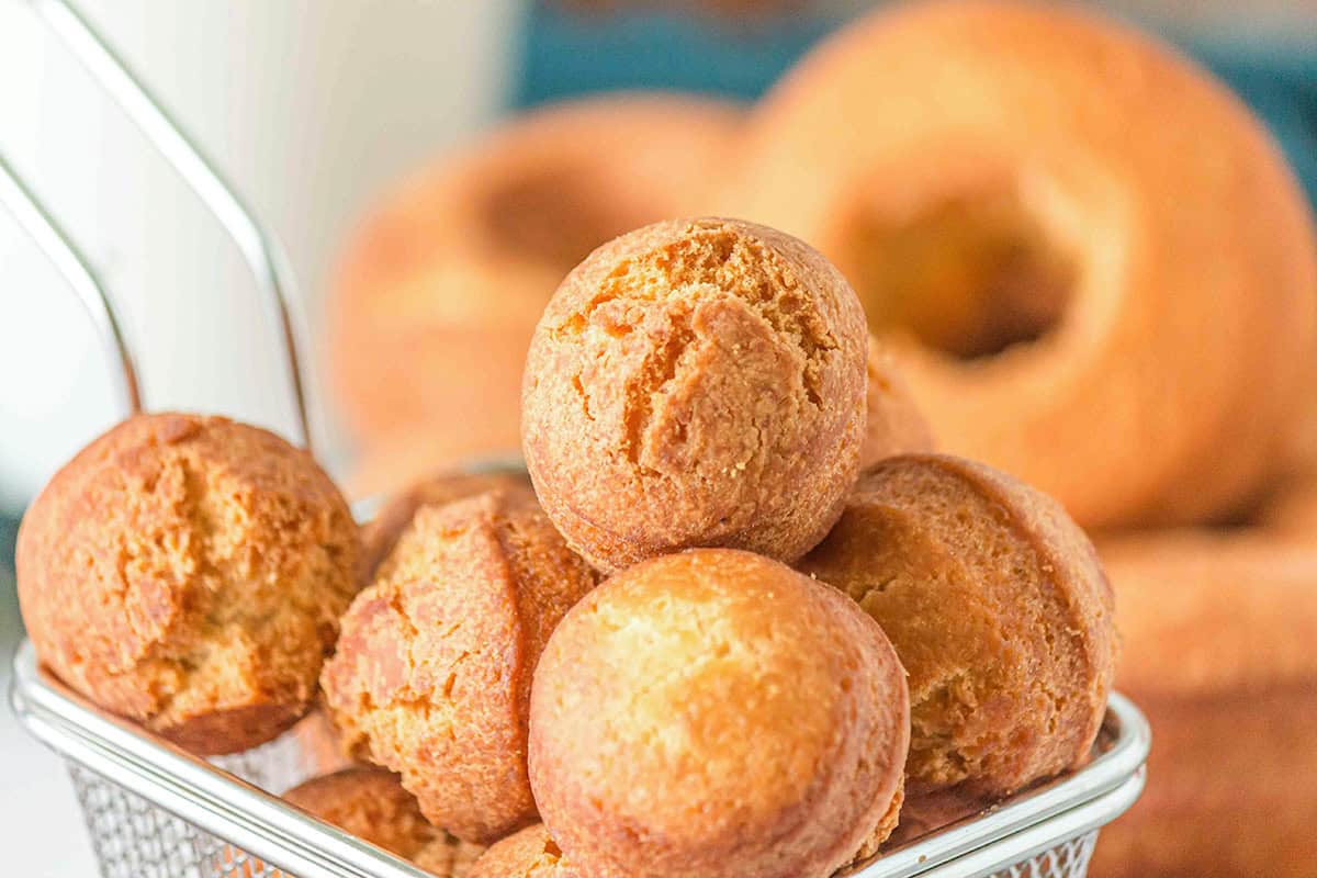A metal basket filled with round, golden-brown donut holes sits in front of several Homemade Cake Donuts arranged in the background.