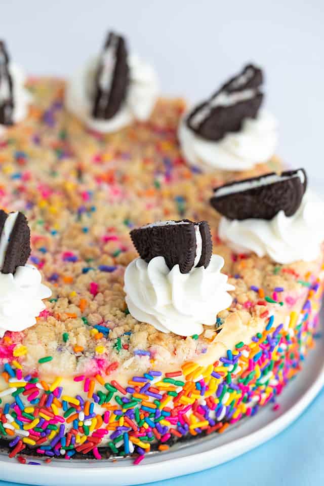 Birthday Cheesecake - This birthday cheesecake is packed full of flavor! It has a birthday cake Oreo cookie crust, a cheesecake batter with a cake batter extract and bits of sugar cookie dough in it. The top has a golden brown sugar cookie crumble. It makes a beautiful sprinkle wrapped birthday cake cheesecake for any cheesecake lover. #cookiedoughandovenmitt #cheesecakerecipes #cheesecake #birthdaycake #sugarcookies #dessertrecipes
