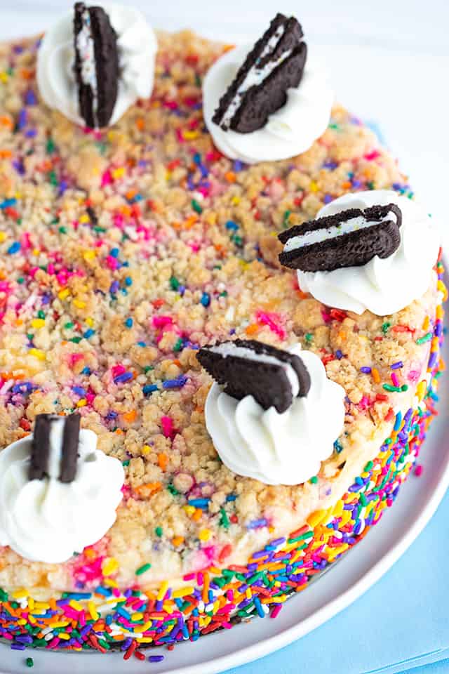 Birthday Cheesecake - This birthday cheesecake is packed full of flavor! It has a birthday cake Oreo cookie crust, a cheesecake batter with a cake batter extract and bits of sugar cookie dough in it. The top has a golden brown sugar cookie crumble. It makes a beautiful sprinkle wrapped birthday cake cheesecake for any cheesecake lover. #cookiedoughandovenmitt #cheesecakerecipes #cheesecake #birthdaycake #sugarcookies #dessertrecipes