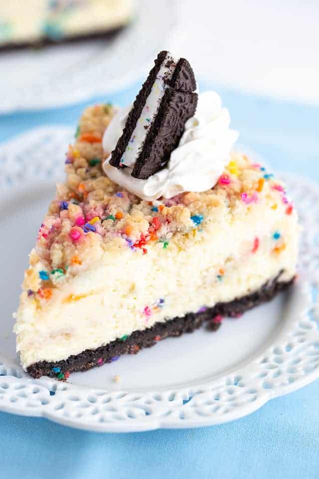 Birthday Cheesecake - This birthday cheesecake is packed full of flavor! It has a birthday cake Oreo cookie crust, a cheesecake batter with a cake batter extract and bits of sugar cookie dough in it. The top has a golden brown sugar cookie crumble. It makes a beautiful sprinkle wrapped birthday cake cheesecake for any cheesecake lover. #cookiedoughandovenmitt #cheesecakerecipes #cheesecake #birthdaycake #sugarcookies #dessertrecipes