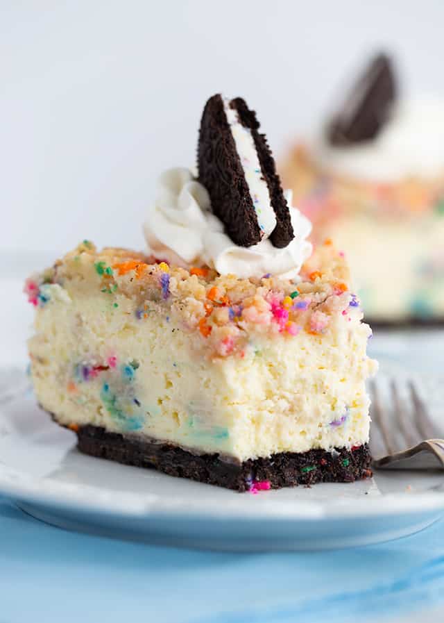 Birthday Cheesecake - This birthday cheesecake is packed full of flavor! It has a birthday cake Oreo cookie crust, a cheesecake batter with a cake batter extract and bits of sugar cookie dough in it. The top has a golden brown sugar cookie crumble. It makes a beautiful sprinkle wrapped birthday cake cheesecake for any cheesecake lover. #cookiedoughandovenmitt #cheesecakerecipes #cheesecake #birthdaycake #sugarcookies #dessertrecipes
