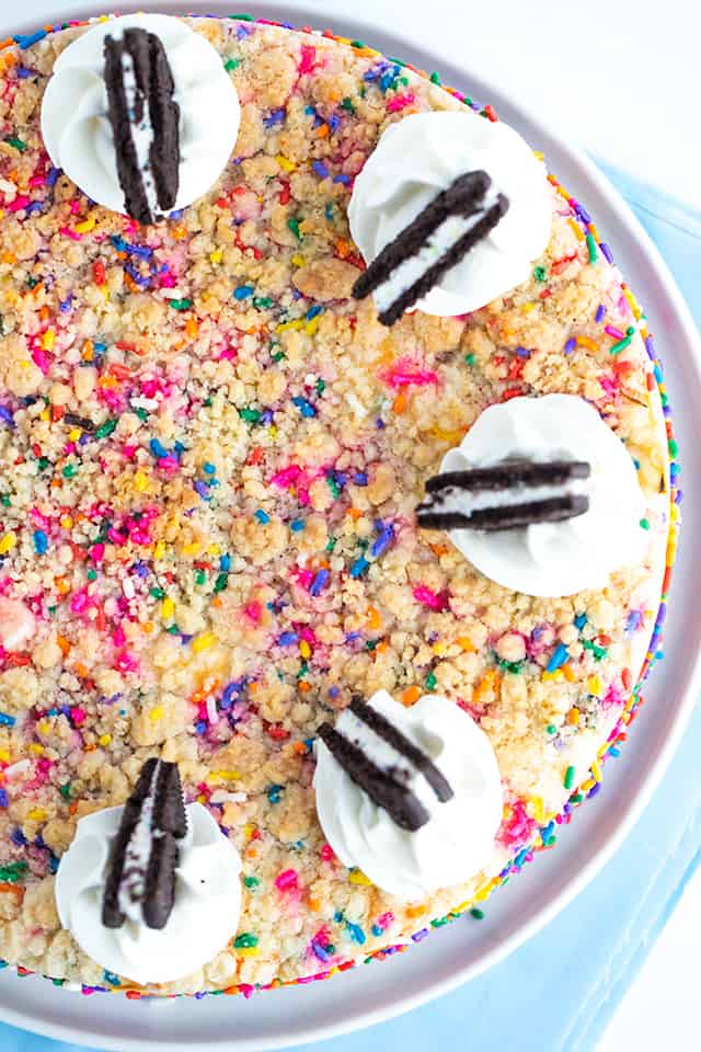 Birthday Cheesecake - This birthday cheesecake is packed full of flavor! It has a birthday cake Oreo cookie crust, a cheesecake batter with a cake batter extract and bits of sugar cookie dough in it. The top has a golden brown sugar cookie crumble. It makes a beautiful sprinkle wrapped birthday cake cheesecake for any cheesecake lover. #cookiedoughandovenmitt #cheesecakerecipes #cheesecake #birthdaycake #sugarcookies #dessertrecipes