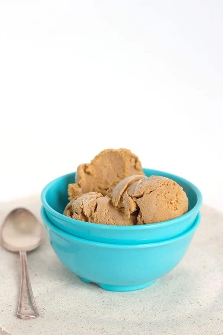 Two scoops of pumpkin pie ice cream in a bright blue bowl next to a silver spoon.