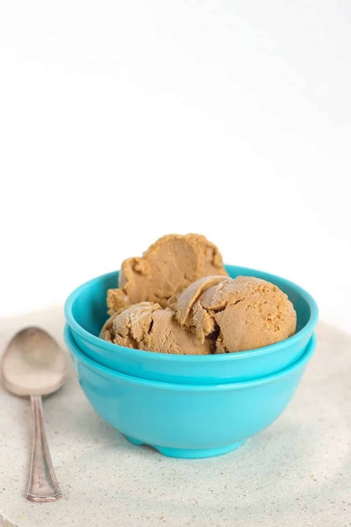 Two scoops of pumpkin pie ice cream in a bright blue bowl next to a silver spoon.