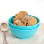 Three scoops of pumpkin pie ice cream in a bright blue bowl with a metal spoon beside it.