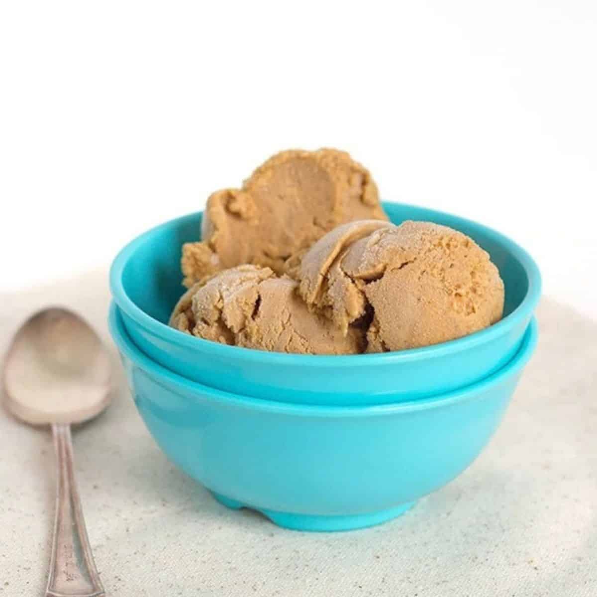 Three scoops of pumpkin pie ice cream in a bright blue bowl with a metal spoon beside it.