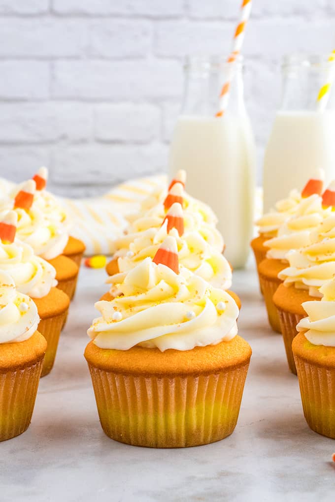 A group of candy corn cupcakes with frosting and a glass of milk.