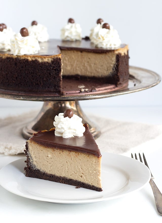 slice of mocha cheesecake on a white plate with cheesecake on a cake platter behind it