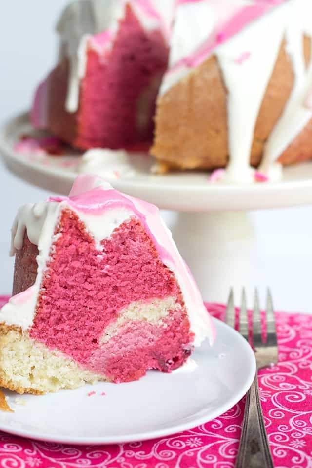 A Raspberry Vanilla Pink Ombre Bundt Cake with a slice taken out.
