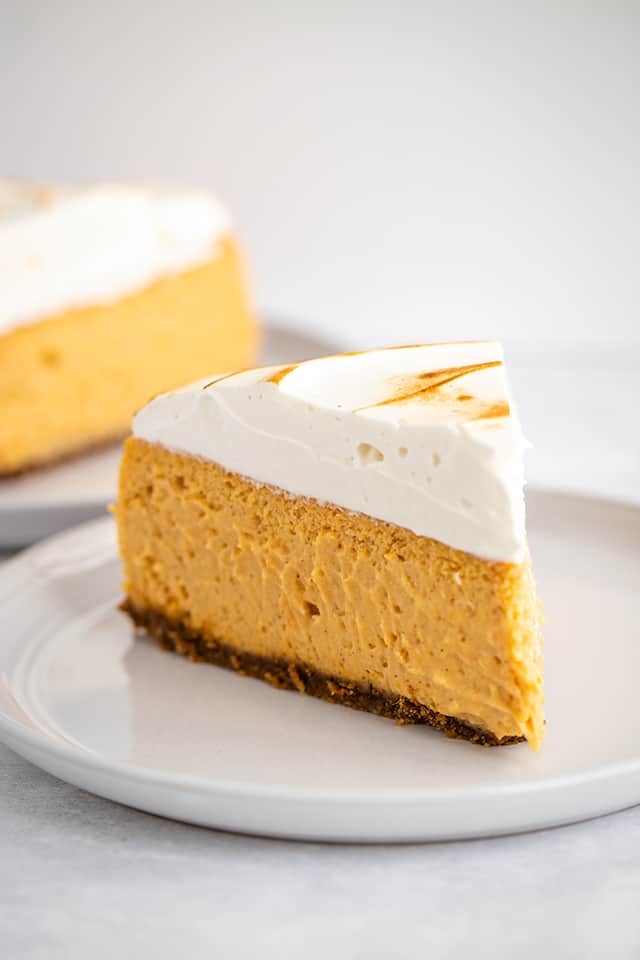 slice of sweet potato cheesecake on white plate with a slice of cheesecake behind it
