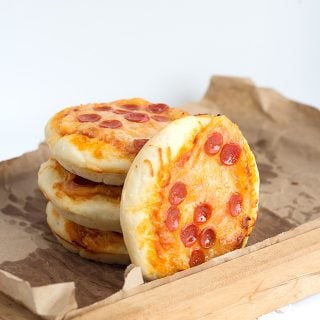 A stack of mini pizzas on a wooden cutting board.