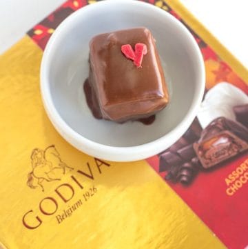 Box of Godiva chocolates with a heart-shaped chocolate and strawberry petit fours.