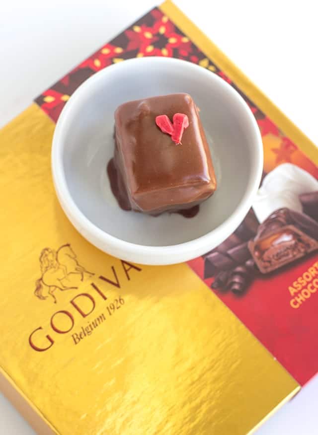 Box of Godiva chocolates with a heart-shaped chocolate and strawberry petit fours.