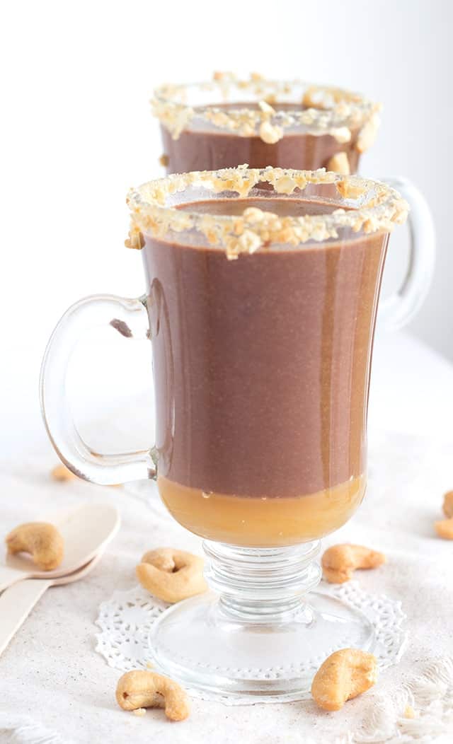 Two mugs filled with hot cocoa and cashews.