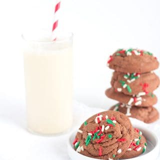 A plate of chocolate sugar cookies with sprinkles and a glass of milk.