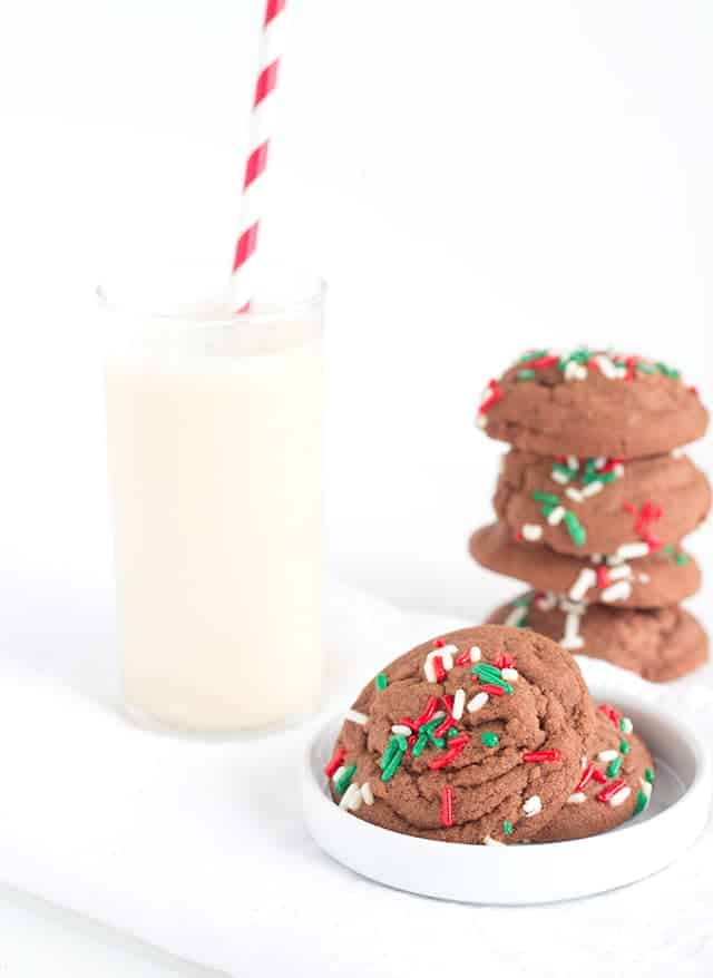 A plate of chocolate sugar cookies with sprinkles and a glass of milk.