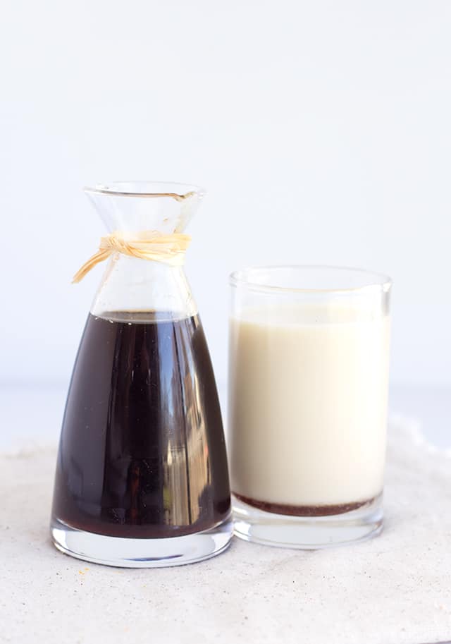 glass carafe filled with simple coffee syrup sits next to a glass of milk