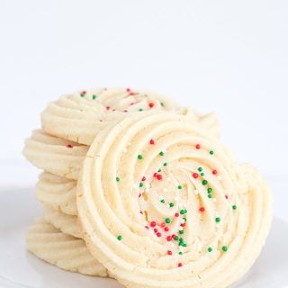 Spritz cookies with sprinkles displayed on a white plate.