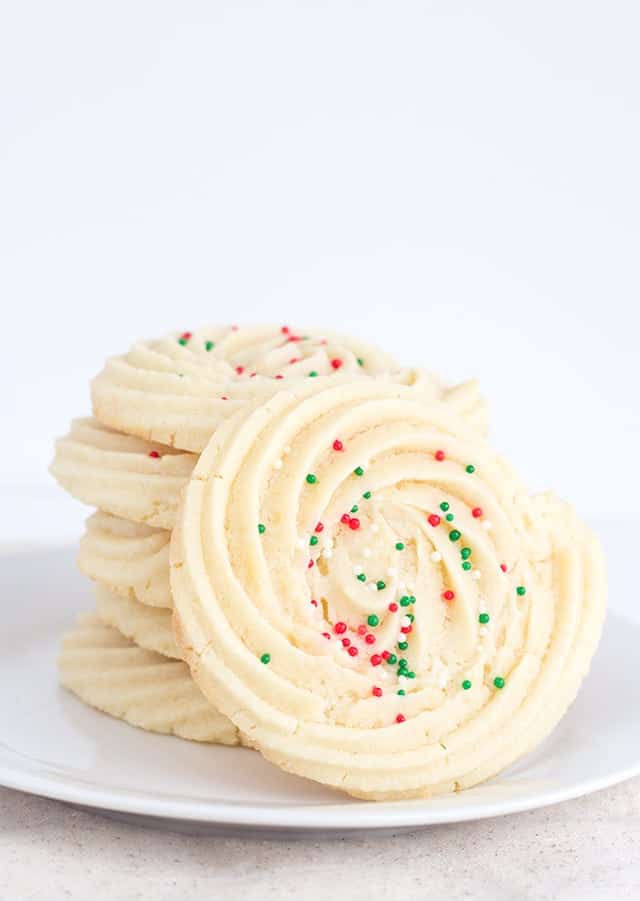 Spritz cookies with sprinkles displayed on a white plate.