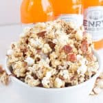 A bowl of maple bacon popcorn with soda bottles.