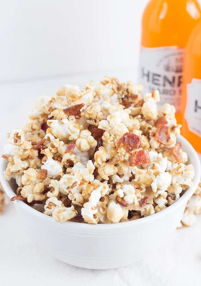 Henry's maple bacon popcorn in a white bowl with a bottle of Henry's.