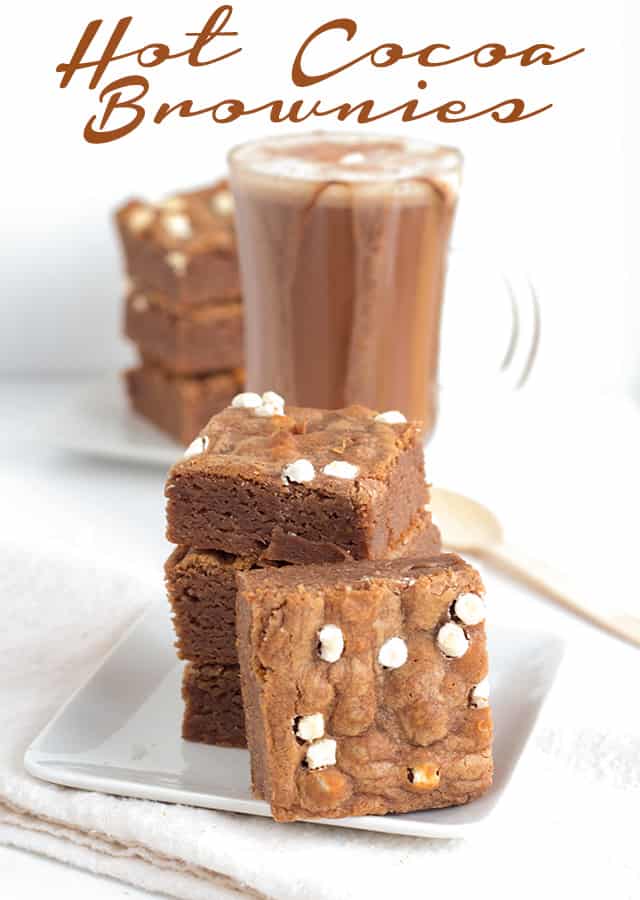 Hot Cocoa Brownies are chewy brownies, packed full of hot cocoa and tiny marshmallows bits. Make this easy cocoa brownies recipe and enjoy them with a mug of hot chocolate! stack of brownies with one in front showing off the meringue top and mallow bits