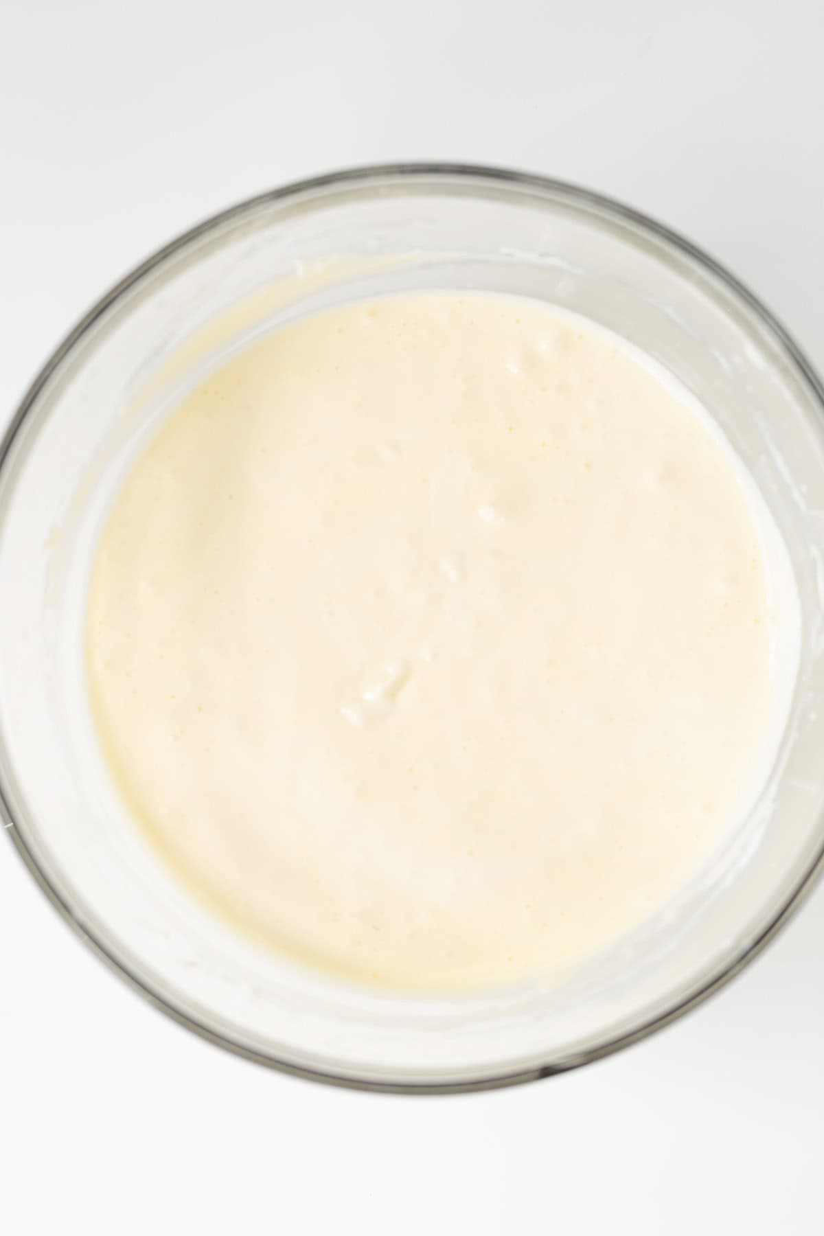 A glass bowl filled with smooth, pale yellow batter&mdash;perfect for making Strawberry Cheesecake Bars&mdash;is seen from above on a white background.