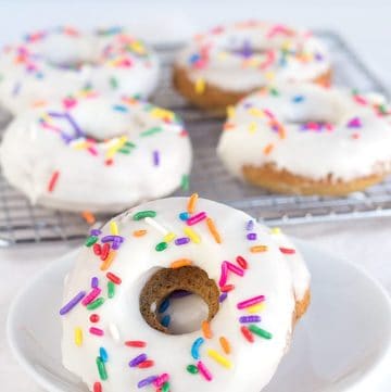 Baked vanilla donuts with sprinkles and icing on a white plate.