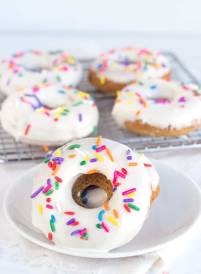 Baked vanilla donuts with sprinkles and icing on a white plate.