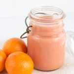 A jar of blood orange curd with oranges next to it.