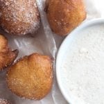Fried banana fritters with powdered sugar and a bowl of dipping sauce.