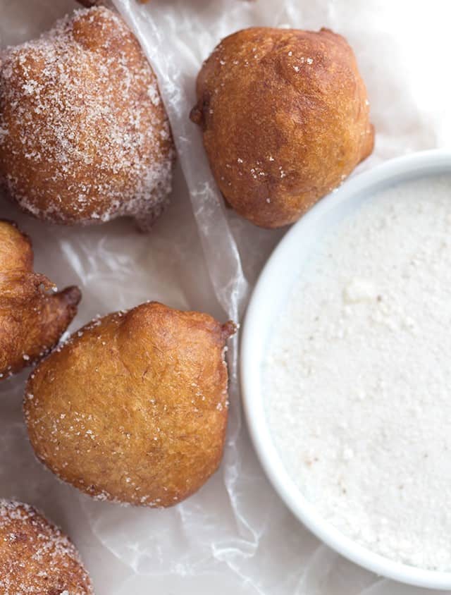 Fried banana fritters with powdered sugar and a bowl of dipping sauce.