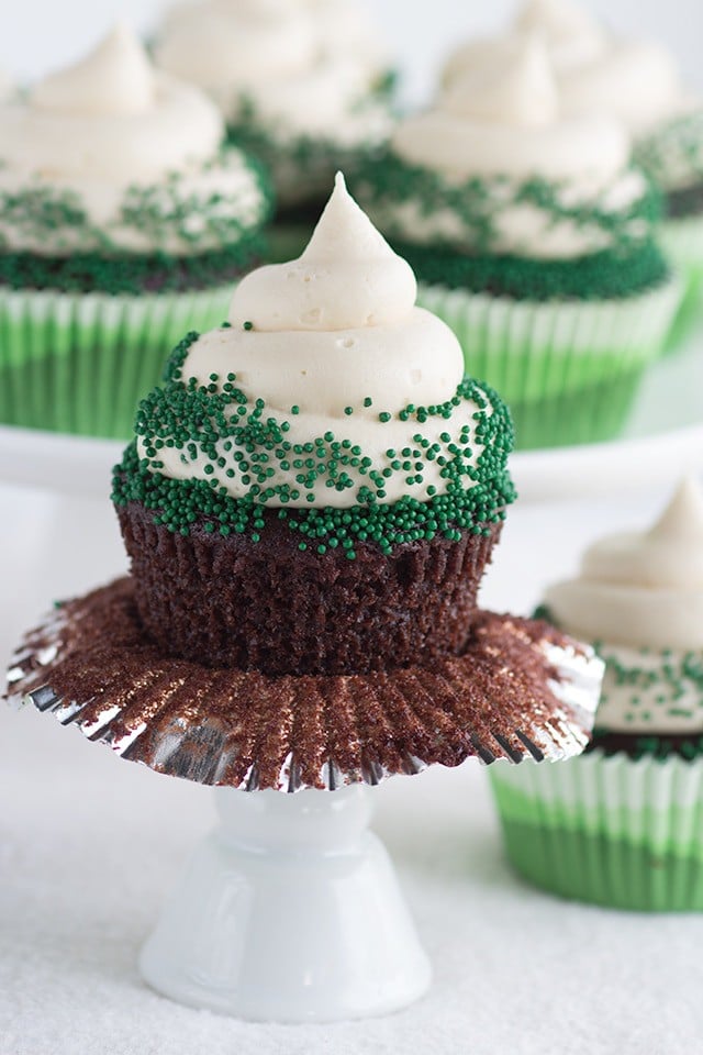 One Chocolate Guinness Cupcake with Baileys Cream Cheese Frosting and green nonpariels with the cupcake liner partially unwrapped from around the cupcake