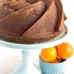 A bundt cake with oranges on a cake stand.