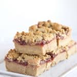 A stack of raspberry bars drizzled with peanut butter on a white plate.
