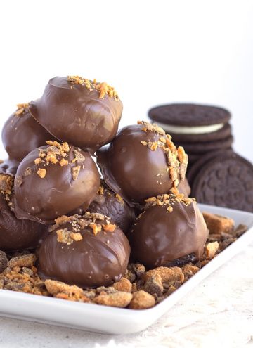 stack of butterfinger bites with crushed candy bars and white square plate with a stack of cookies
