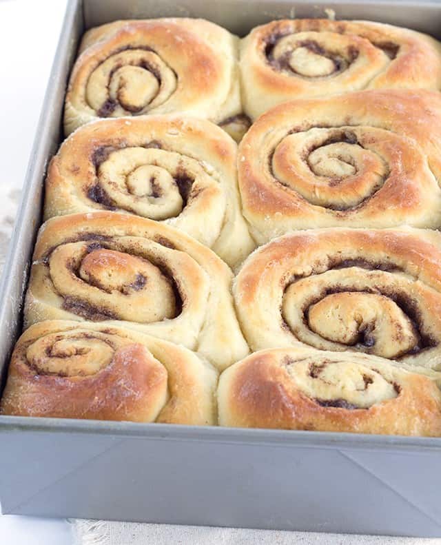 Gooey cinnamon rolls in a pan on a table.